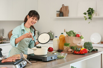 Young woman making noodle soup in kitchen