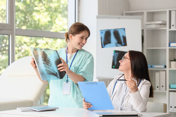 Female doctor with assistant studying x-ray image of lungs at table in clinic