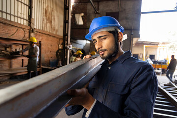 Industrial worker carrying iron strips on his shoulders at factory