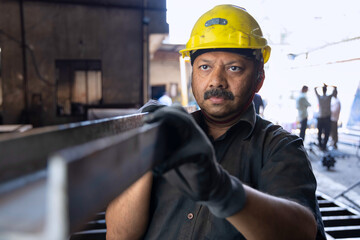 Industrial worker carrying iron strips on his shoulders at factory