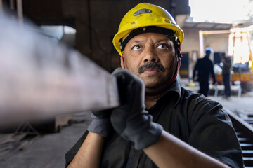 Industrial worker carrying iron strips on his shoulders at factory