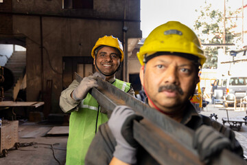 Industrial worker carrying iron strips on his shoulders at factory