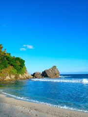 Tropical beach with white sand, clear blue sea, rocky cliffs, and lush greenery under bright summer sky – perfect exotic travel and vacation destination background