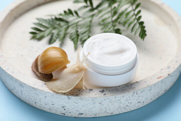 Giant Achatina snail, tray and jar of cosmetic product on blue background, closeup