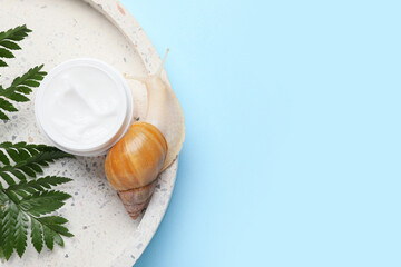 Giant Achatina snail, tray and jar of cosmetic product on blue background, closeup