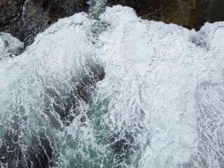 Aerial view of strong ocean waves crashing on rocky coastline, creating foamy white surf and...
