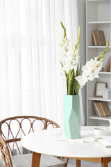Vase with gladiolus flowers on dining table in room