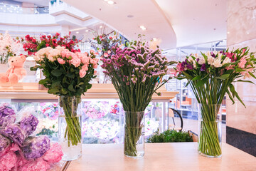 Fresh bouquets of pink roses, purple static, and colorful alstroemeria in glass vases at a floral shop. Flower market display for gifting and celebration.