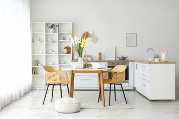 Interior of light kitchen with counters, dining table and gladiolus flowers