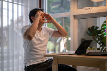 Stressed asian businessman massaging temples at home office desk