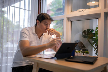 Focused asian freelancer working from home using tablet and stylus