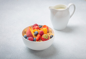 Healthy breakfast with oatmeal porridge with peach, strawberry, raspberry, blueberry and milk in white bowl on gray background, perfect for a nutritious and energizing start to the day