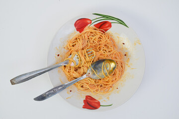 A plate of messy spaghetti with a few stray strands tangled around a spoon and fork, set against a...