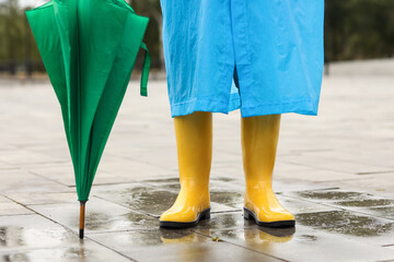 Legs of man in blue raincoat with gumboots and umbrella outdoors