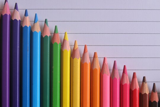 Rainbow colored pencils aligned by height on lined paper, back to school, art supplies, education concept.