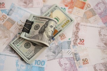 Bunch of US dollar bills lies on big amount of Brazilian reais banknotes close up