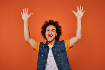 A cheerful young person with curly hair raises their arms in excitement, enjoying a vibrant moment