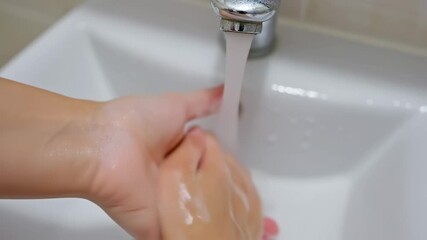 A person carefully washes their hands under a running faucet in a clean white sink. The video highlights the importance of personal hygiene and proper handwashing to maintain good health and cleanline