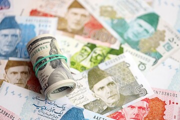 Roll of US dollar bills lies on big amount of Pakistan rupees banknotes close up