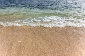 foamy waves washing up onto a sandy beach, with a clear separation between the sand and water.