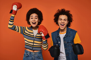 Joyful young friends celebrate victory in boxing gloves against a vibrant orange backdrop