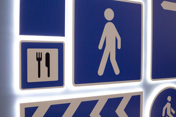 Various directional and informational signs. Symbols include pedestrian icon, dining symbol with...