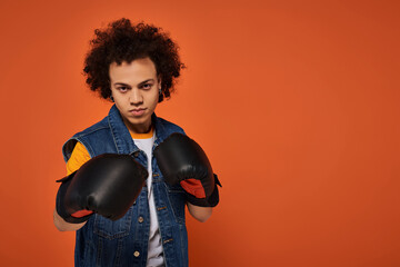 Young person with curly hair and boxing gloves showcasing style against vibrant orange background