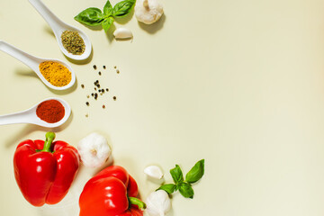 Spoons with spices, red bell peppers, garlic, basil and black peppercorns on olive background. Natural products, vegetables, culinary ingredients, food background for cooking and advertising.