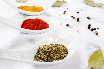 Close-up of spoons with bright aromatic spices, black peppercorns and bay leaves on marble...