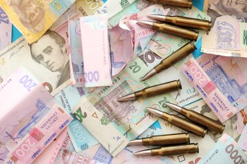 Many rifle bullets lies on lots of ukrainian money bills close up