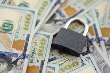 Small black padlock lies on big amount of new hundred US dollar bills