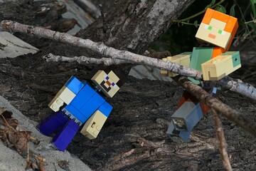 Naklejka premium LEGO Minecraft large figures of Steve and Alex climbing on dried fallen broadleaf tree branches on sandy bank of Danube river, southern Slovakia. 