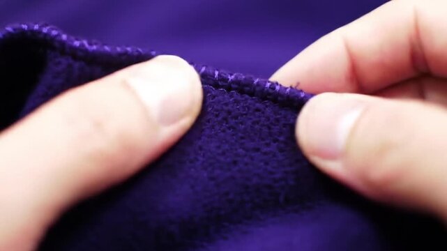 Fingers holding purple fabric with tight overlock stitching, suitable for fashion design, textiles, sewing, crafting, and product photography projects.