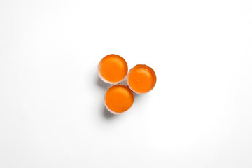 Three raw egg yolks in brown shells arranged neatly, top-down on a bright white background for a modern minimal look.