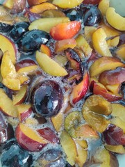 A close-up shows cut plums of various colors simmering in a sugary liquid, bubbles rise to the surface as they cook into delicious homemade jam in Russia