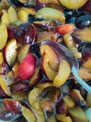 Plum slices simmer in a pot, stirred occasionally with a spoon. The process of turning fresh fruit into flavorful jam fills the kitchen with warmth and sweet fragrance