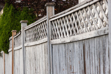 Aged and peeling white wooden fence with decorative lattice trim, showing signs of weathering and...