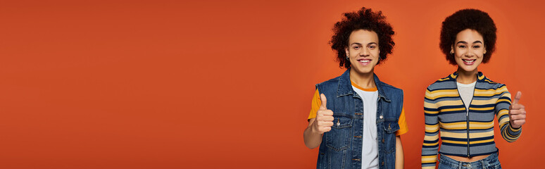 Young fashion lovers flaunt vibrant styles on a bold orange backdrop with playful smiles