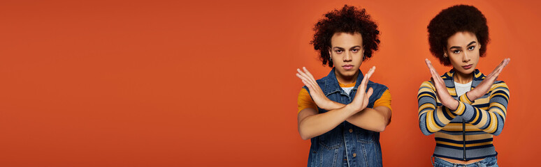 Two young models with curly hair express their unique fashion sense in a lively orange background
