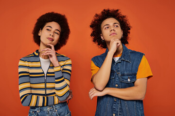 Young individuals with curly hair showcase unique fashion styles against a vibrant orange backdrop