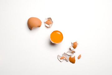 Flat-lay of three yolks in half shells with scattered shell fragments on a white background, clean...