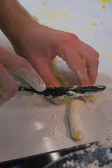 A person uses a knife to cut a long piece of gnocchi dough into individual pieces on a floured...