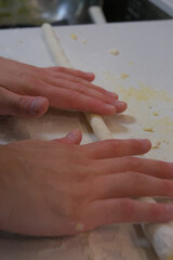 A person uses their hands to roll a log of gnocchi dough on a floured white countertop, preparing it to be cut.