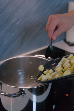 A person uses a spoon to slide raw potato gnocchi from a baking sheet into a pot of boiling water on a stove.