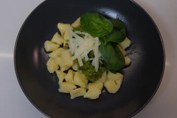 A close-up shot of green pesto made with pistachios and fresh basil in a clear glass on a kitchen countertop.