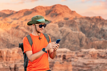 Young traveler using a mobile phone while enjoying the breathtaking sunset over the mountains, surrounded by stunning desert landscapes
