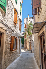 A charming narrow alley in a historic Mediterranean old town, with traditional stone houses and colorful wooden shutters on a sunny day with shadows and light playing on the ancient stone facades