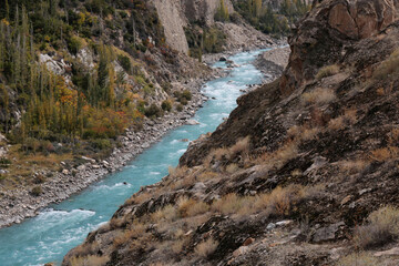A turquoise mountain river winds through a rocky canyon with cliffs, boulders and autumnal trees along its banks.