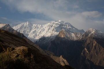 Fototapeta premium Snowcapped mountain range with rugged rocky foreground beneath a dramatic cloudy sky, an alpine panorama evoking remote, highaltitude wilderness.