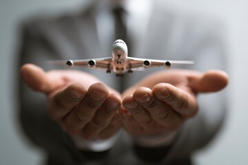 A person in a suit holds a toy airplane in their cupped hands presented towards the viewer